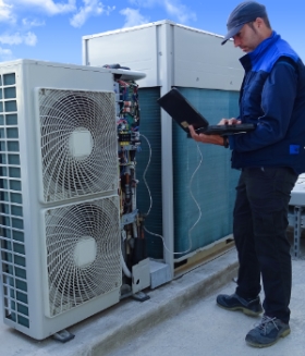 HVAC technician making a diagnosis of an industrial air conditioning unit with a laptop on a rooftop